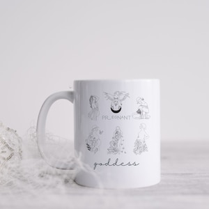 May include: White ceramic mug with black line drawings of women in various poses, including pregnant, with flowers, and with wings. The text "PREGNANT" and "goddess" are printed on the mug.
