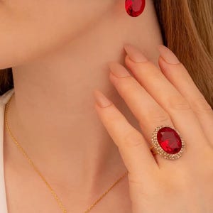 Peut inclure: Un collier en or avec un pendentif en forme de larme rouge, une paire de boucles d'oreilles assorties et une bague avec une grande pierre ovale rouge.