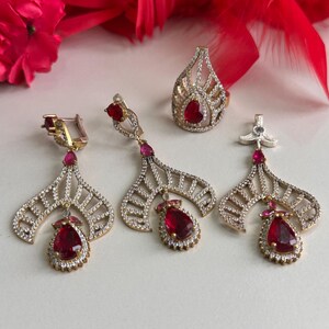 May include: A set of silver earrings and a ring with red gemstone accents. The jewelry features a delicate, intricate design with a teardrop-shaped pendant.