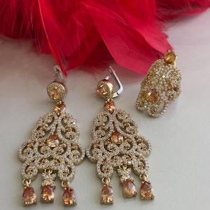 May include: A set of gold-tone earrings and a ring with a delicate filigree design and orange-colored stones.