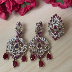 May include: A set of gold-tone earrings and a ring with a filigree design and red and clear stones.