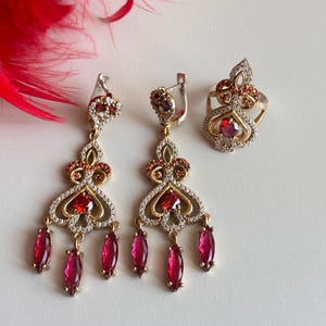 May include: A set of silver earrings and a ring with red and clear stones. The earrings have a dangling design with multiple red stones.