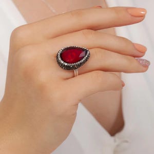May include: A silver ring with a large red pear-shaped gemstone surrounded by smaller black gemstones.