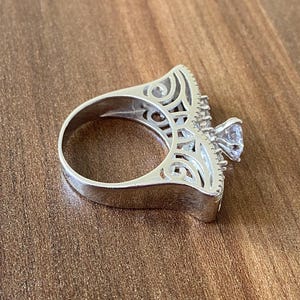 May include: A silver ring with a large, clear stone set in a filigree design.