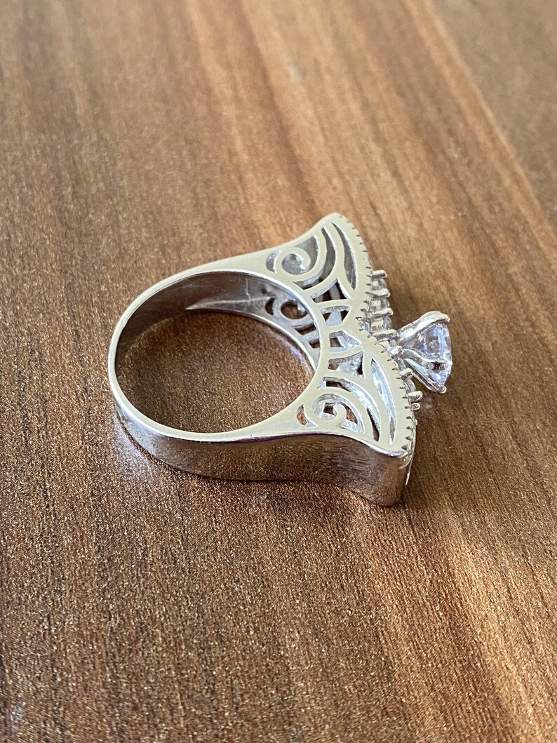 May include: A silver ring with a large, clear stone set in a filigree design.