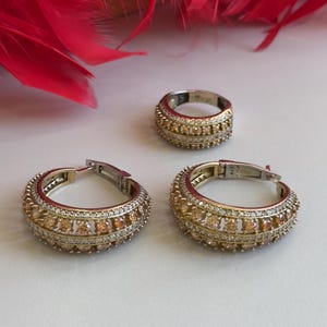 May include: A set of gold and silver hoop earrings and a ring with clear and amber colored stones.