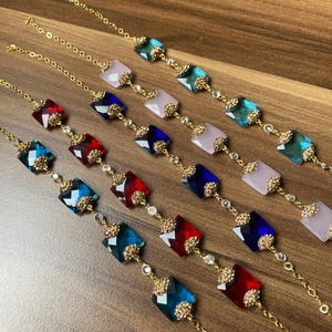May include: Five gold chain bracelets with different coloured square-shaped crystal charms. The charms are blue, red and pink.