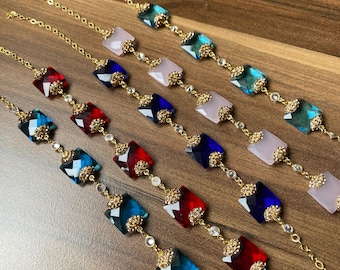 Pode incluir: Cinco pulseiras de corrente dourada com diferentes pingentes de cristal quadrados coloridos. Os pingentes são azuis, vermelhos e rosados.