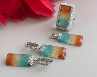 Puede incluir: Un conjunto de pendientes de plata y un anillo con una piedra rectangular multicolor. La piedra es un degradado de verde, naranja y amarillo.