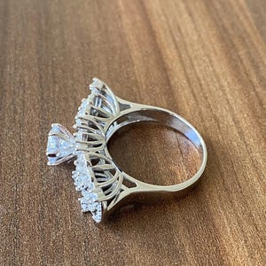 May include: A silver ring with a large, clear, round gemstone surrounded by smaller, clear gemstones. The ring has a delicate, intricate design.