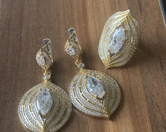 Könnte beinhalten: Ein goldfarbener Schmuck-Set mit einem Ring und Ohrringen. Der Ring und die Ohrringe haben einen großen, klaren, markisenförmigen Stein, der von kleineren Steinen umgeben ist.