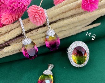 Puede incluir: Un conjunto de joyas con un anillo, pendientes y un colgante. Las piezas tienen una piedra preciosa multicolor en forma de lágrima con tonos rosas, amarillos y morados. El anillo y los pendientes están rodeados de pequeñas piedras transparentes. También se incluye el colgante.