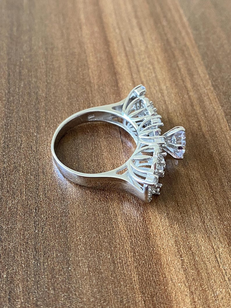 May include: A silver ring with a large, clear center stone and smaller stones set in a delicate, intricate design.