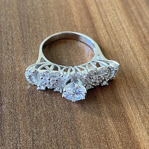 May include: A silver ring with a large, clear center stone and smaller stones set in a delicate, intricate design.
