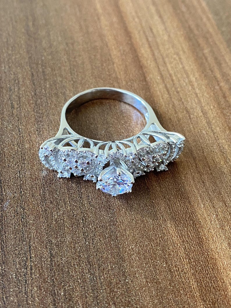 May include: A silver ring with a large, clear center stone and smaller stones set in a delicate, intricate design.