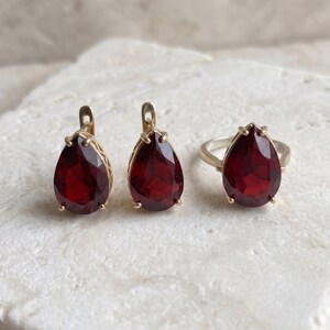 Peut inclure: Un ensemble de bijoux composé de deux boucles d'oreilles en forme de goutte et d'une bague assortie, chacune dotée d'une grande pierre précieuse rouge foncé à facettes, montée sur une monture en métal doré avec des griffes.