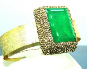 Pode incluir: Um bracelete de ouro com uma grande gema verde esmeralda engastada em uma moldura quadrada de pedras transparentes brilhantes.