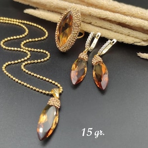 Puede incluir: Un conjunto de joyas doradas con collar, anillo y pendientes. El collar tiene un colgante con una piedra preciosa de color ámbar. El anillo y los pendientes también presentan piedras preciosas de color ámbar. La imagen incluye el texto "15 gr."