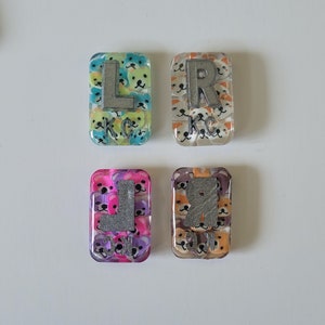 May include: Four colourful eye chart tiles with a cartoon animal print background. Each tile has a silver letter, L, R, L, and R.