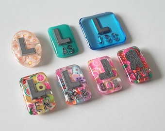May include: Assortment of colourful resin letter charms with different patterns, including flowers, fruit, and confetti. The letters are L, R, and J.S.C.