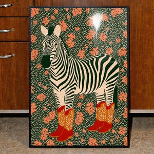 May include: A framed art print featuring a zebra with black and white stripes, wearing red cowboy boots. The background is a green floral pattern with orange flowers. The artwork is displayed in a kitchen setting.
