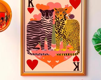 May include: A framed artwork depicts a zebra and a leopard on a heart-shaped card. The sofa has a leopard print pattern and is adorned with pink, cream, and red pillows. A camera sits on a small table.