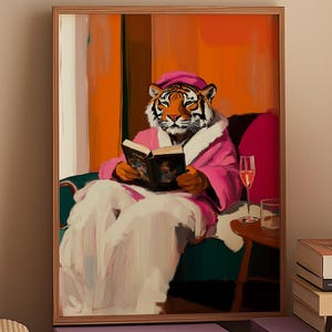 May include: A tiger wearing a pink robe and holding a book sits in a chair. The tiger is looking at the book. The background is a warm orange color.