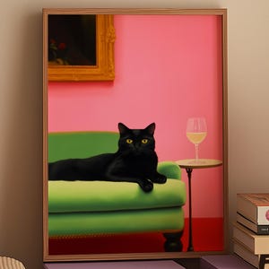 Pode incluir: Uma impressão emoldurada com um gato preto deitado em um sofá verde contra uma parede rosa. Uma pequena mesa segura uma taça de vinho. Uma pintura com moldura dourada está pendurada na parede. Uma lâmpada cor de pêssego está em uma pilha de livros.