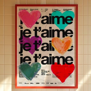 May include: A red framed poster with the text "j'aime je t'aime je t'aime" in black. The poster features five colorful hearts in various shades of red, pink, green, and blue.