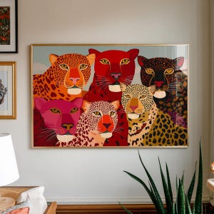 May include: A framed art print featuring six stylized leopard faces in vibrant colors. The leopards have orange, red, pink, and black spots and fur. The artwork is displayed in a gold frame and hangs on a white wall.