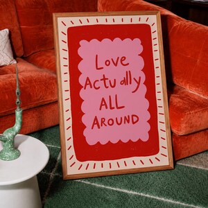 A playful pink and red typography print featuring the hand-lettered message “Love Actually All Around” inside a scalloped frame. The warm peach background, bold lettering and imperfect drawn texture give the artwork a cheerful, handmade character. Designed for bedrooms, living rooms, gallery walls or an above-bed display, this romantic wall art adds color without feeling overly formal. A thoughtful choice for anniversaries, Valentine’s Day, newlyweds or anyone who loves expressive quote posters.