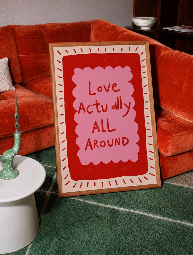 A playful pink and red typography print featuring the hand-lettered message “Love Actually All Around” inside a scalloped frame. The warm peach background, bold lettering and imperfect drawn texture give the artwork a cheerful, handmade character. Designed for bedrooms, living rooms, gallery walls or an above-bed display, this romantic wall art adds color without feeling overly formal. A thoughtful choice for anniversaries, Valentine’s Day, newlyweds or anyone who loves expressive quote posters.