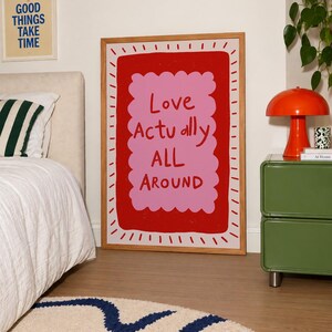 A playful pink and red typography print featuring the hand-lettered message “Love Actually All Around” inside a scalloped frame. The warm peach background, bold lettering and imperfect drawn texture give the artwork a cheerful, handmade character. Designed for bedrooms, living rooms, gallery walls or an above-bed display, this romantic wall art adds color without feeling overly formal. A thoughtful choice for anniversaries, Valentine’s Day, newlyweds or anyone who loves expressive quote posters.