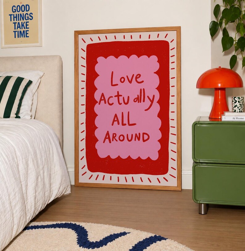 A playful pink and red typography print featuring the hand-lettered message “Love Actually All Around” inside a scalloped frame. The warm peach background, bold lettering and imperfect drawn texture give the artwork a cheerful, handmade character. Designed for bedrooms, living rooms, gallery walls or an above-bed display, this romantic wall art adds color without feeling overly formal. A thoughtful choice for anniversaries, Valentine’s Day, newlyweds or anyone who loves expressive quote posters.