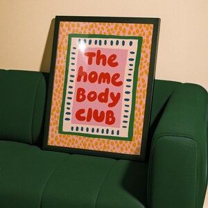 Playful typography poster featuring the phrase The Home Body Club in bold red lettering on a soft pink background. Framed with green and cream borders and surrounded by mustard yellow abstract dots, this colorful maximalist design blends cozy lifestyle humor with eclectic pattern layering and retro-inspired charm.Home Body Poster, Typography Wall Art, Cozy Quote Print, Maximalist Decor, Eclectic Print, Retro Style Poster, Entryway Wall Decor, Bold Letter Art, Trendy Art Print, Dopamine Color Art