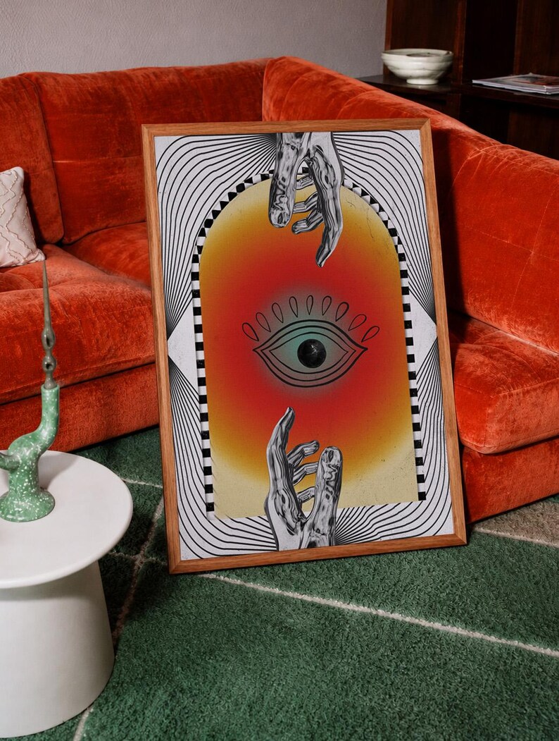 May include: A framed rectangular wall art print featuring a central archway with a gradient orange and yellow background. Inside the arch is a black line drawing of an eye, positioned between two reaching hands. The border has black and white lines.
