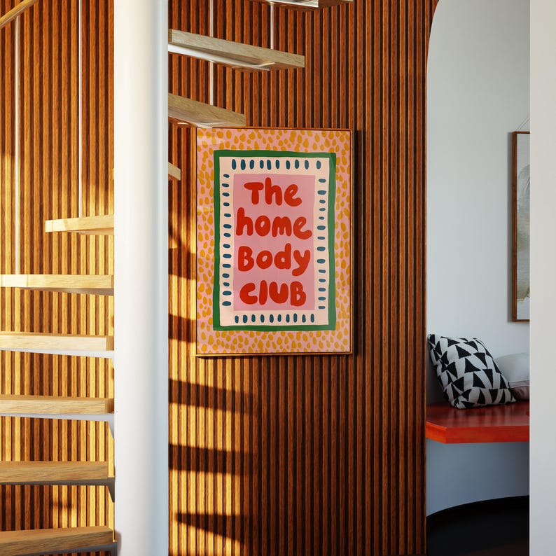 Playful typography poster featuring the phrase The Home Body Club in bold red lettering on a soft pink background. Framed with green and cream borders and surrounded by mustard yellow abstract dots, this colorful maximalist design blends cozy lifestyle humor with eclectic pattern layering and retro-inspired charm.Home Body Poster, Typography Wall Art, Cozy Quote Print, Maximalist Decor, Eclectic Print, Retro Style Poster, Entryway Wall Decor, Bold Letter Art, Trendy Art Print, Dopamine Color Art