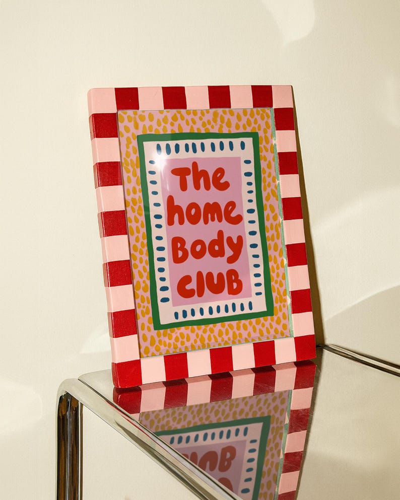 Playful typography poster featuring the phrase The Home Body Club in bold red lettering on a soft pink background. Framed with green and cream borders and surrounded by mustard yellow abstract dots, this colorful maximalist design blends cozy lifestyle humor with eclectic pattern layering and retro-inspired charm.Home Body Poster, Typography Wall Art, Cozy Quote Print, Maximalist Decor, Eclectic Print, Retro Style Poster, Entryway Wall Decor, Bold Letter Art, Trendy Art Print, Dopamine Color Art