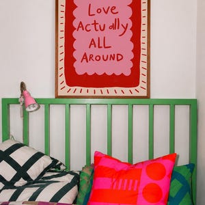 A playful pink and red typography print featuring the hand-lettered message “Love Actually All Around” inside a scalloped frame. The warm peach background, bold lettering and imperfect drawn texture give the artwork a cheerful, handmade character. Designed for bedrooms, living rooms, gallery walls or an above-bed display, this romantic wall art adds color without feeling overly formal. A thoughtful choice for anniversaries, Valentine’s Day, newlyweds or anyone who loves expressive quote posters.