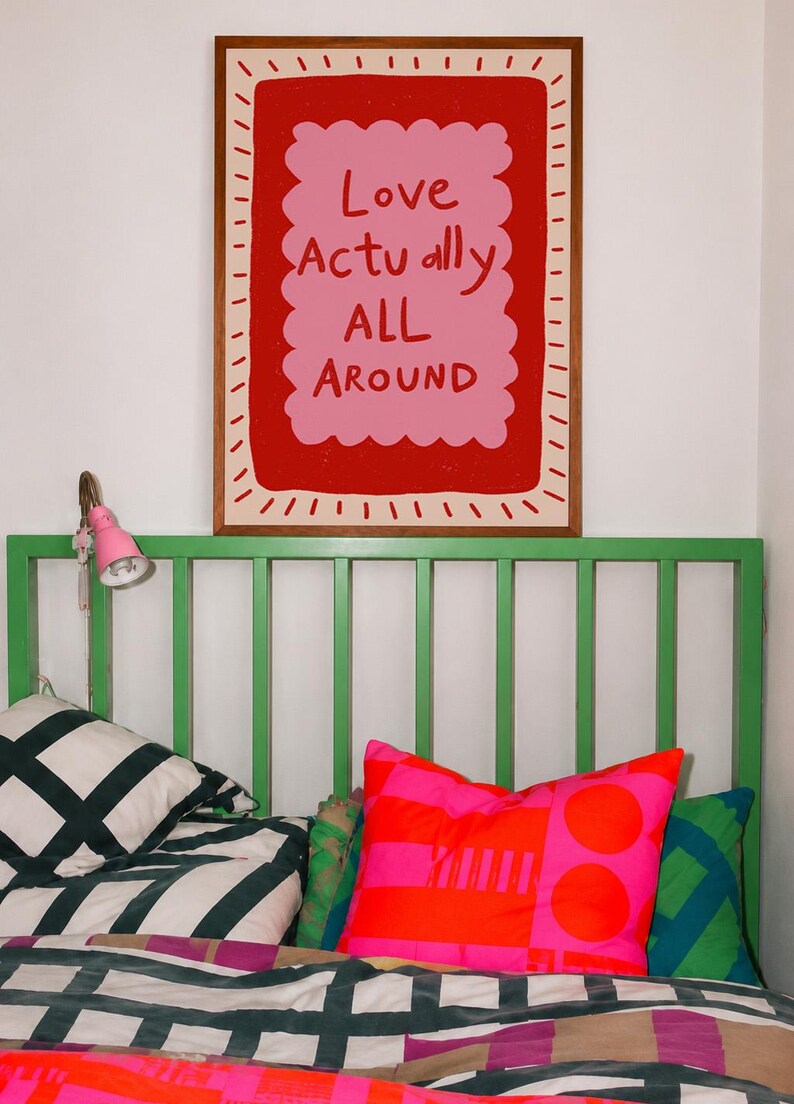 A playful pink and red typography print featuring the hand-lettered message “Love Actually All Around” inside a scalloped frame. The warm peach background, bold lettering and imperfect drawn texture give the artwork a cheerful, handmade character. Designed for bedrooms, living rooms, gallery walls or an above-bed display, this romantic wall art adds color without feeling overly formal. A thoughtful choice for anniversaries, Valentine’s Day, newlyweds or anyone who loves expressive quote posters.