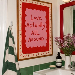 A playful pink and red typography print featuring the hand-lettered message “Love Actually All Around” inside a scalloped frame. The warm peach background, bold lettering and imperfect drawn texture give the artwork a cheerful, handmade character. Designed for bedrooms, living rooms, gallery walls or an above-bed display, this romantic wall art adds color without feeling overly formal. A thoughtful choice for anniversaries, Valentine’s Day, newlyweds or anyone who loves expressive quote posters.