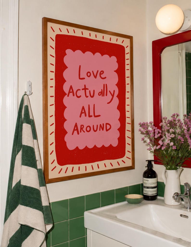 A playful pink and red typography print featuring the hand-lettered message “Love Actually All Around” inside a scalloped frame. The warm peach background, bold lettering and imperfect drawn texture give the artwork a cheerful, handmade character. Designed for bedrooms, living rooms, gallery walls or an above-bed display, this romantic wall art adds color without feeling overly formal. A thoughtful choice for anniversaries, Valentine’s Day, newlyweds or anyone who loves expressive quote posters.