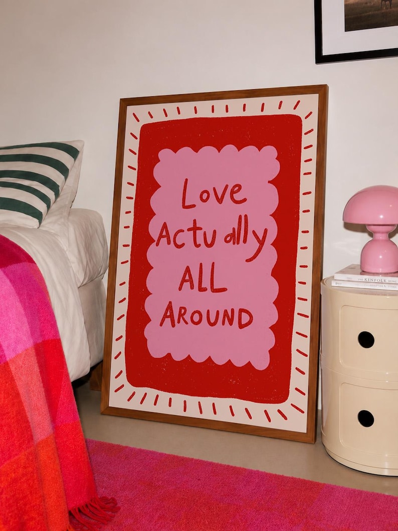 A playful pink and red typography print featuring the hand-lettered message “Love Actually All Around” inside a scalloped frame. The warm peach background, bold lettering and imperfect drawn texture give the artwork a cheerful, handmade character. Designed for bedrooms, living rooms, gallery walls or an above-bed display, this romantic wall art adds color without feeling overly formal. A thoughtful choice for anniversaries, Valentine’s Day, newlyweds or anyone who loves expressive quote posters.
