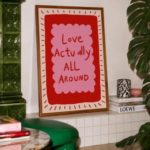 A playful pink and red typography print featuring the hand-lettered message “Love Actually All Around” inside a scalloped frame. The warm peach background, bold lettering and imperfect drawn texture give the artwork a cheerful, handmade character. Designed for bedrooms, living rooms, gallery walls or an above-bed display, this romantic wall art adds color without feeling overly formal. A thoughtful choice for anniversaries, Valentine’s Day, newlyweds or anyone who loves expressive quote posters.