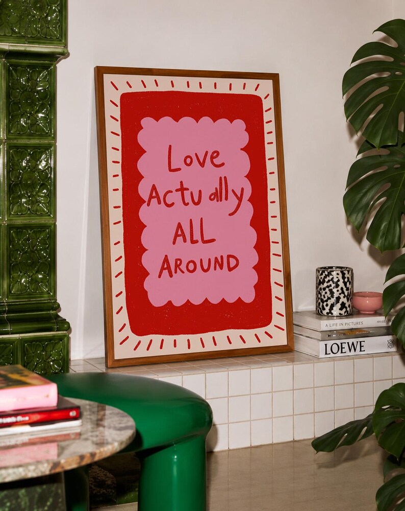 A playful pink and red typography print featuring the hand-lettered message “Love Actually All Around” inside a scalloped frame. The warm peach background, bold lettering and imperfect drawn texture give the artwork a cheerful, handmade character. Designed for bedrooms, living rooms, gallery walls or an above-bed display, this romantic wall art adds color without feeling overly formal. A thoughtful choice for anniversaries, Valentine’s Day, newlyweds or anyone who loves expressive quote posters.