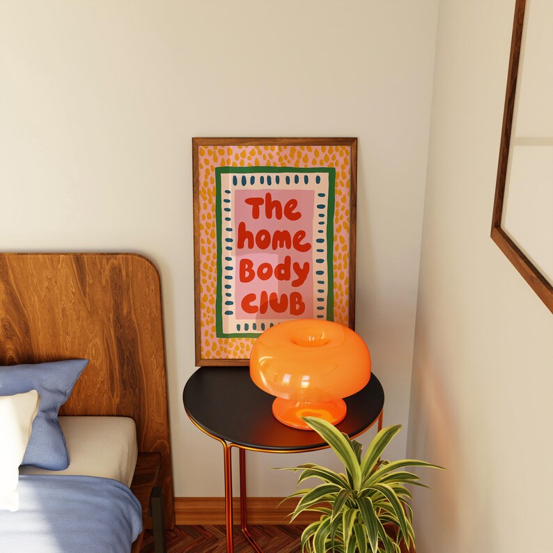 Playful typography poster featuring the phrase The Home Body Club in bold red lettering on a soft pink background. Framed with green and cream borders and surrounded by mustard yellow abstract dots, this colorful maximalist design blends cozy lifestyle humor with eclectic pattern layering and retro-inspired charm.Home Body Poster, Typography Wall Art, Cozy Quote Print, Maximalist Decor, Eclectic Print, Retro Style Poster, Entryway Wall Decor, Bold Letter Art, Trendy Art Print, Dopamine Color Art