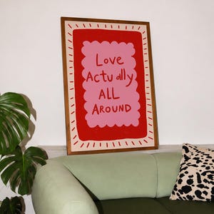 A playful pink and red typography print featuring the hand-lettered message “Love Actually All Around” inside a scalloped frame. The warm peach background, bold lettering and imperfect drawn texture give the artwork a cheerful, handmade character. Designed for bedrooms, living rooms, gallery walls or an above-bed display, this romantic wall art adds color without feeling overly formal. A thoughtful choice for anniversaries, Valentine’s Day, newlyweds or anyone who loves expressive quote posters.