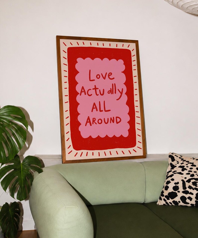 A playful pink and red typography print featuring the hand-lettered message “Love Actually All Around” inside a scalloped frame. The warm peach background, bold lettering and imperfect drawn texture give the artwork a cheerful, handmade character. Designed for bedrooms, living rooms, gallery walls or an above-bed display, this romantic wall art adds color without feeling overly formal. A thoughtful choice for anniversaries, Valentine’s Day, newlyweds or anyone who loves expressive quote posters.