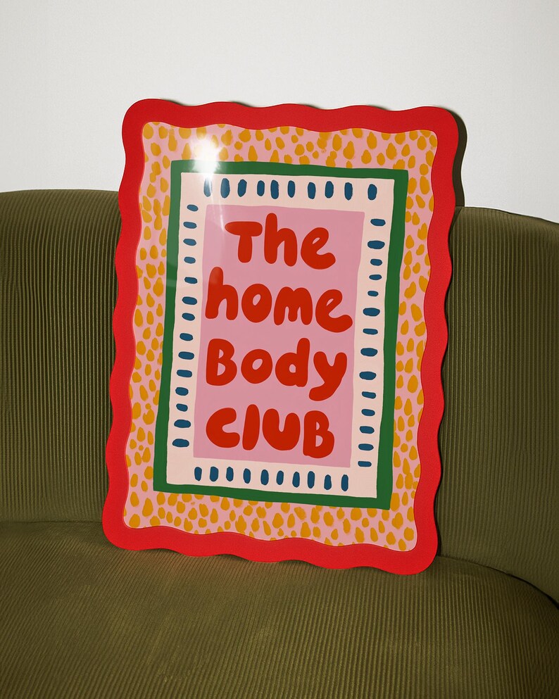 Playful typography poster featuring the phrase The Home Body Club in bold red lettering on a soft pink background. Framed with green and cream borders and surrounded by mustard yellow abstract dots, this colorful maximalist design blends cozy lifestyle humor with eclectic pattern layering and retro-inspired charm.Home Body Poster, Typography Wall Art, Cozy Quote Print, Maximalist Decor, Eclectic Print, Retro Style Poster, Entryway Wall Decor, Bold Letter Art, Trendy Art Print, Dopamine Color Art
