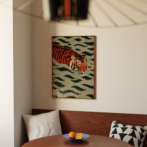 Stylized tiger illustration moving through abstract green wave patterns with dotted textures on a neutral background. The bold orange and black striped tiger contrasts with the rhythmic organic shapes, creating a dynamic maximalist composition. Hand drawn details and modern folk art influences give the artwork a playful yet powerful visual identity. Perfect for living room wall decor, kids room styling, eclectic interiors, or jungle themed spaces seeking a bold statement animal artwork.